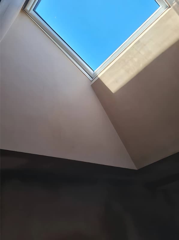 Light falling across a plastered corner beneath a roof window